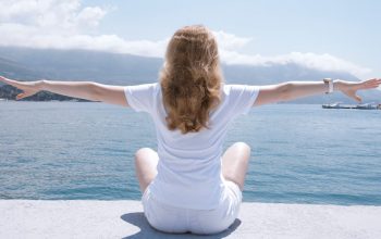 Woman sitting with open arms by the water, embracing nature and serenity.