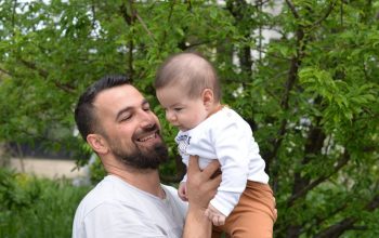 A joyful father lifts his baby in a green, lush outdoor setting.