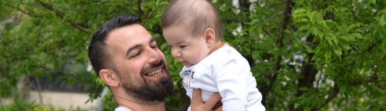 A joyful father lifts his baby in a green, lush outdoor setting.