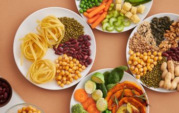A vibrant mix of legumes, vegetables, nuts, and pasta arranged on white plates showcasing a balanced, healthy diet.