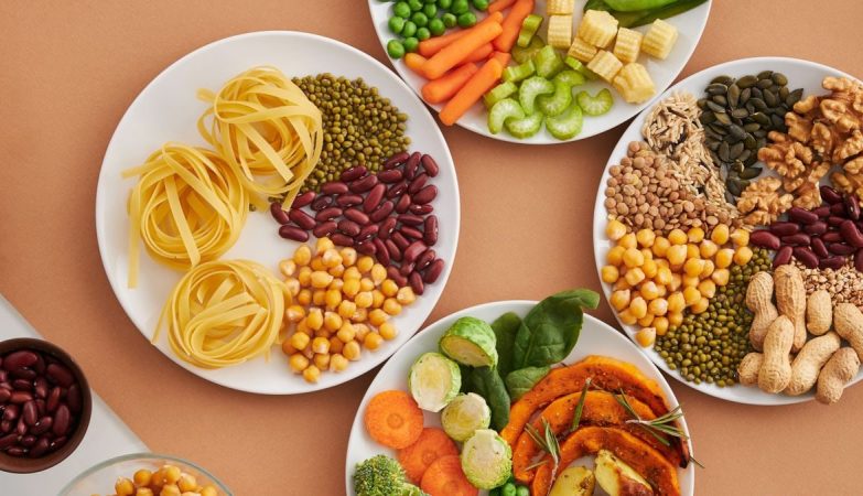 A vibrant mix of legumes, vegetables, nuts, and pasta arranged on white plates showcasing a balanced, healthy diet.